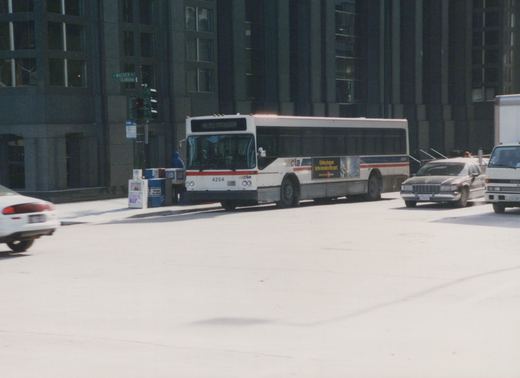 A white CTA bus with the number 4254 is stopped at an intersection in a city, with other vehicles and tall buildings in the background.