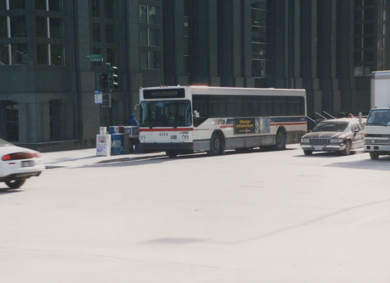 A white CTA bus with the number 4254 is stopped at an intersection in a city, with other vehicles and tall buildings in the background.