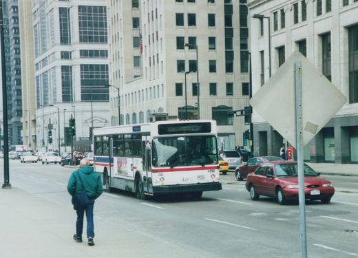 A white and red CTA bus with the number 4260 on its front is driving down a city street lined with tall buildings, with a person walking on the sidewalk.