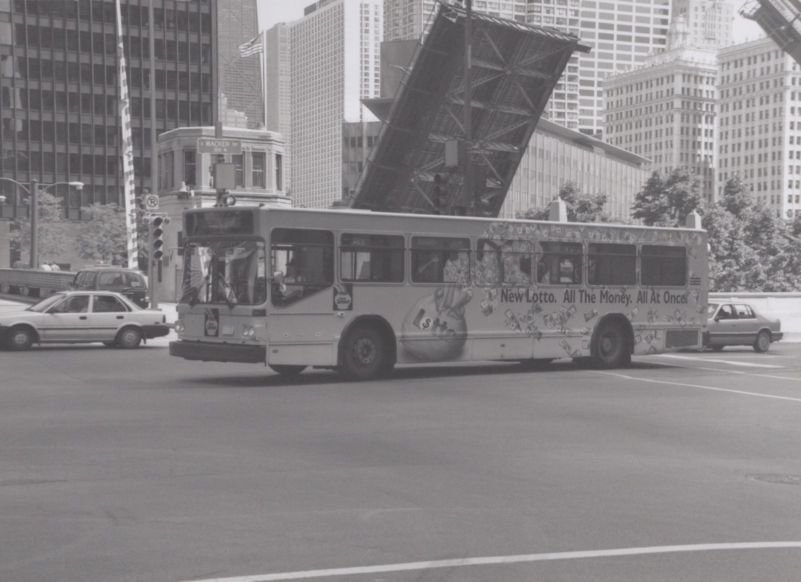 A Chicago Transit Authority bus with the number 4277 is turning on a city street, with skyscrapers and a raised bridge in the background, and an advertisement for 'New Lotto' on its side.