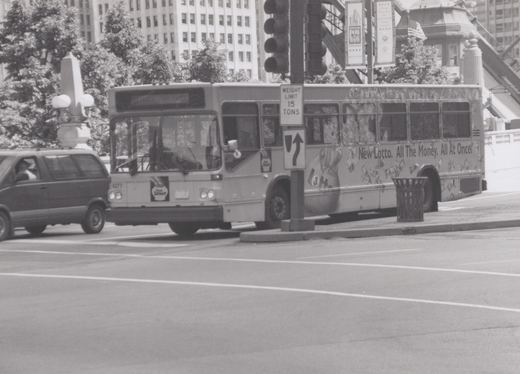 A CTA bus with the number 4277 and an Illinois Lottery ad is stopped on a city street, with a minivan beside it and banners in the background.