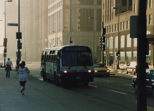 A white and blue Chicago Transit Authority bus with the number 4906 on the front is turning at an intersection with a LaSalle Street sign visible; people are walking and jogging on the sidewalk.