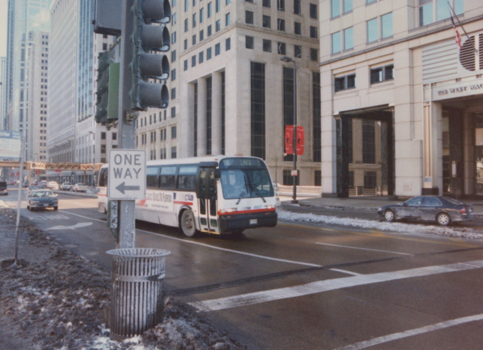 A white and red CTA bus, number 4907, is turning on a snowy street in Chicago with tall buildings and a 'ONE WAY' sign in the foreground.