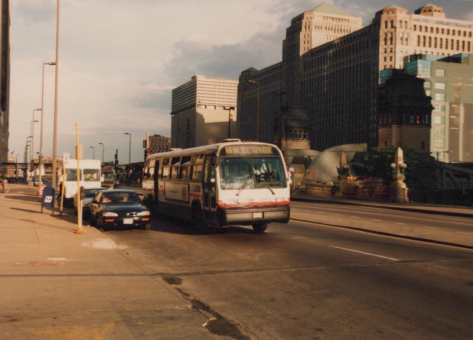 A white and red CTA bus on route 16 to ILL CENTER travels down a city street lined with parked cars and tall office buildings.