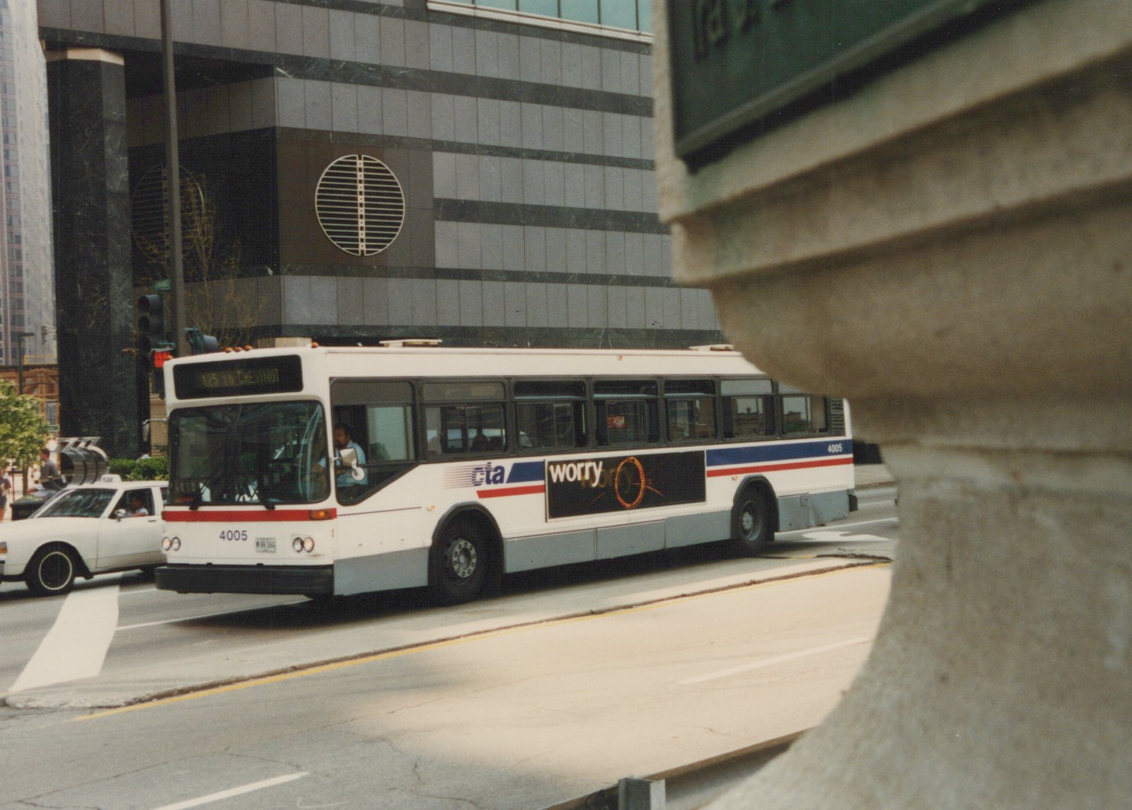 A white Chicago Transit Authority bus with the number 4005 on the front and side, displaying route 125 to Chestnut, is driving on a city street with a modern building in the background.