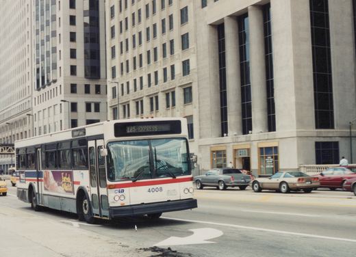 A white, red, and blue Chicago Transit Authority bus with the number 4008 on its front drives down a city street lined with tall buildings and other cars.