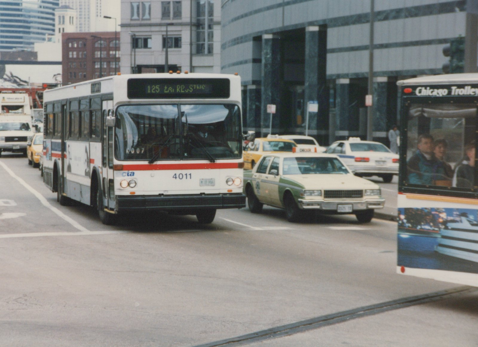 A white Chicago Transit Authority bus with the number 4011 is shown from a three-quarter front view on a city street, with taxis and another bus nearby.