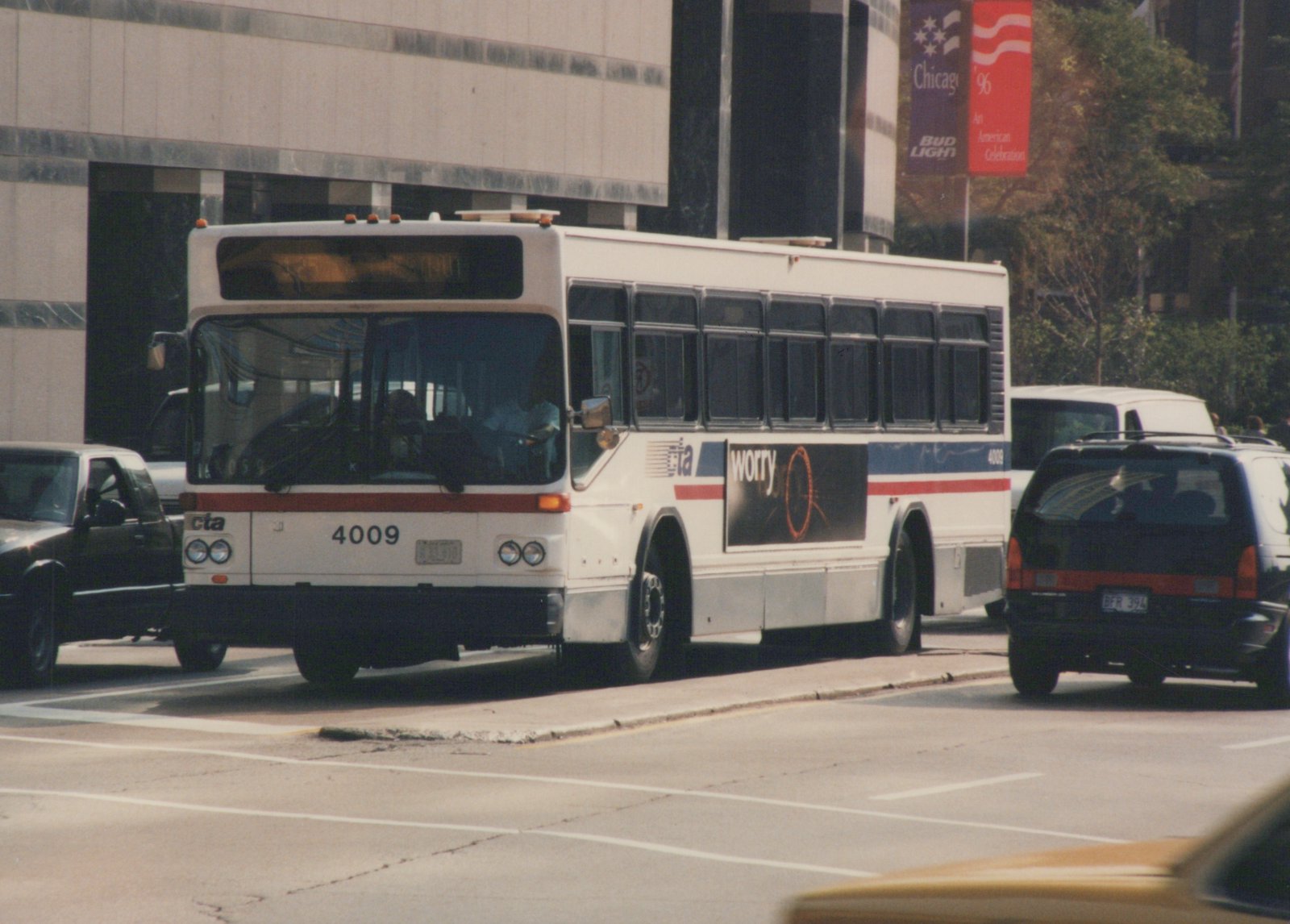 A white CTA bus with the number 4009 is driving down a city street, surrounded by other vehicles, with a large 'Chicago '96' banner visible on a building in the background.