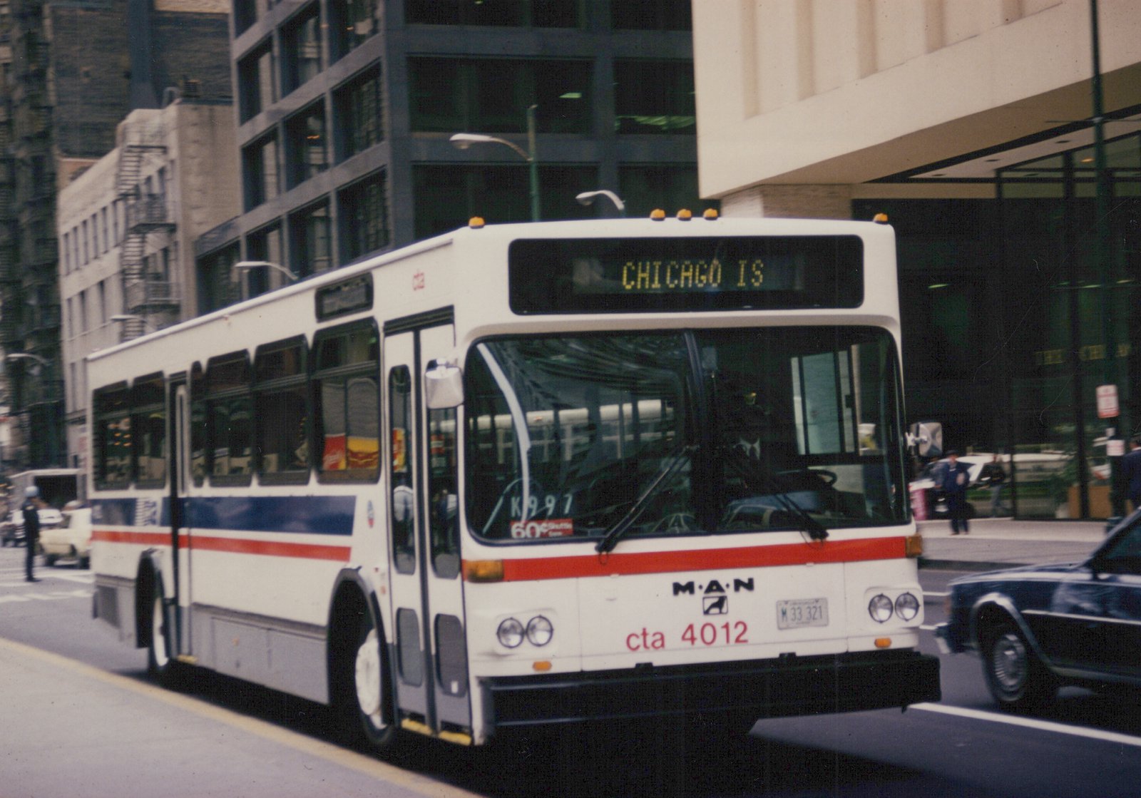 A white and blue Chicago Transit Authority bus with the number 4012 on its front bumper is driving on a city street with tall buildings in the background.