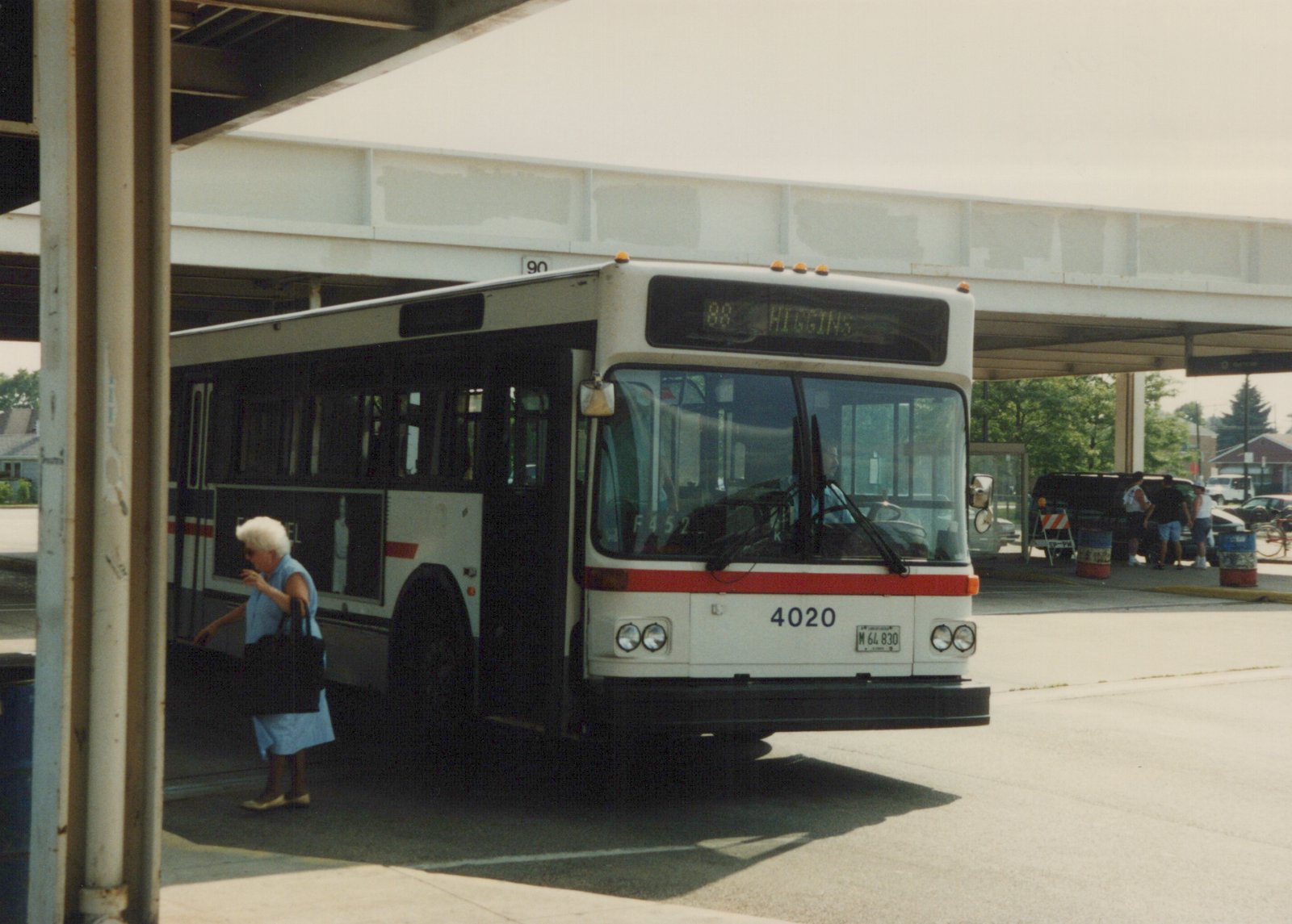 A white and red Chicago Transit Authority bus numbered 4020 is stopped at a terminal under an elevated structure, with passengers nearby and a destination sign reading '88 HIGGINS'.