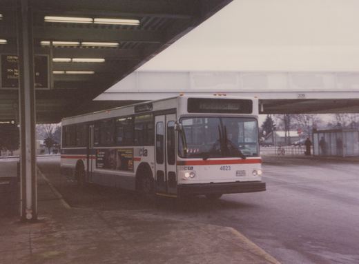 A white and red CTA bus numbered 4023 is parked under a concrete overpass at a bus stop. Two people are visible at a shelter in the background.