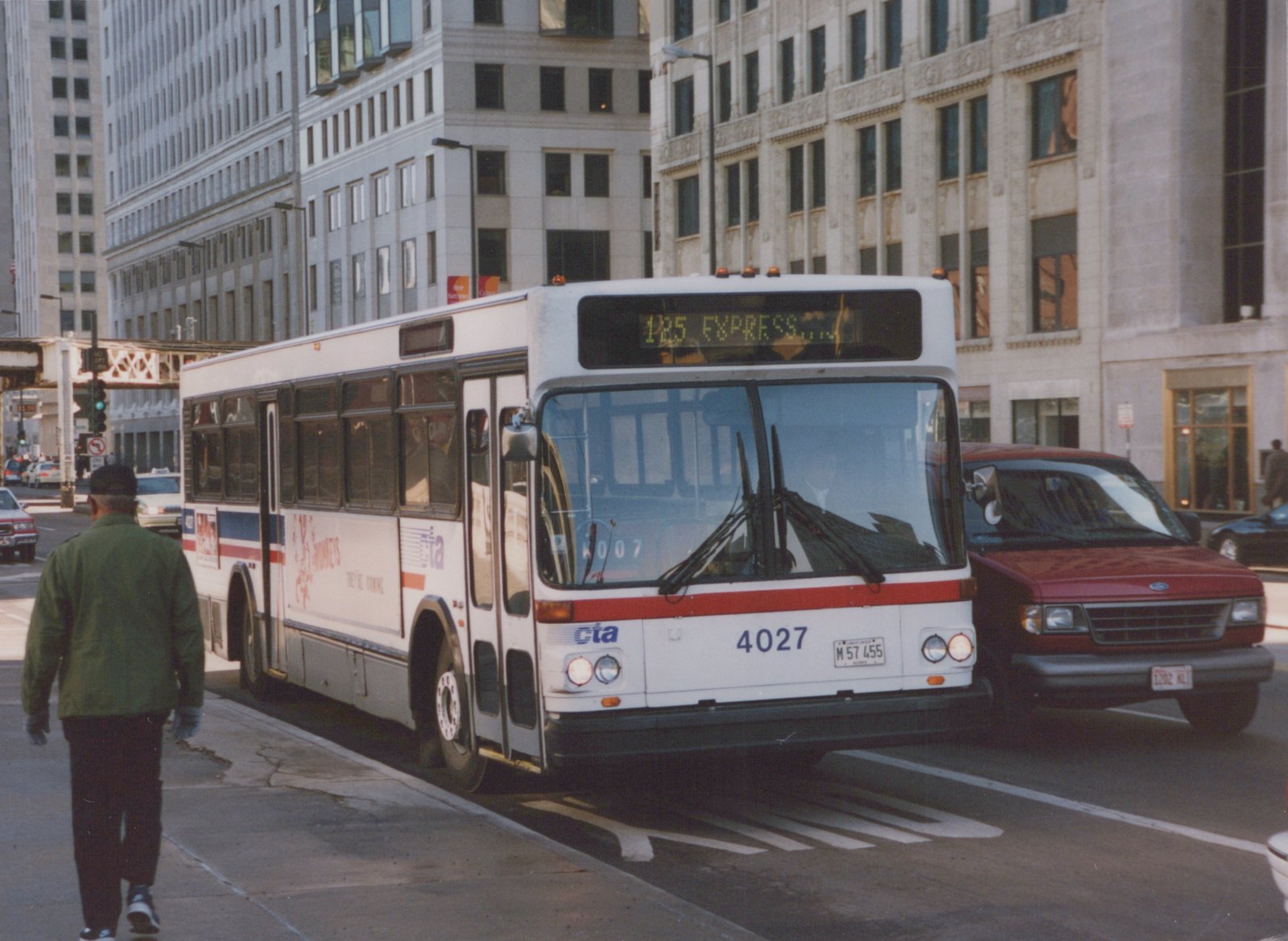 A white Chicago Transit Authority bus with the number 4027 and route 125 Express is driving on a city street, with a pedestrian and other vehicles nearby.