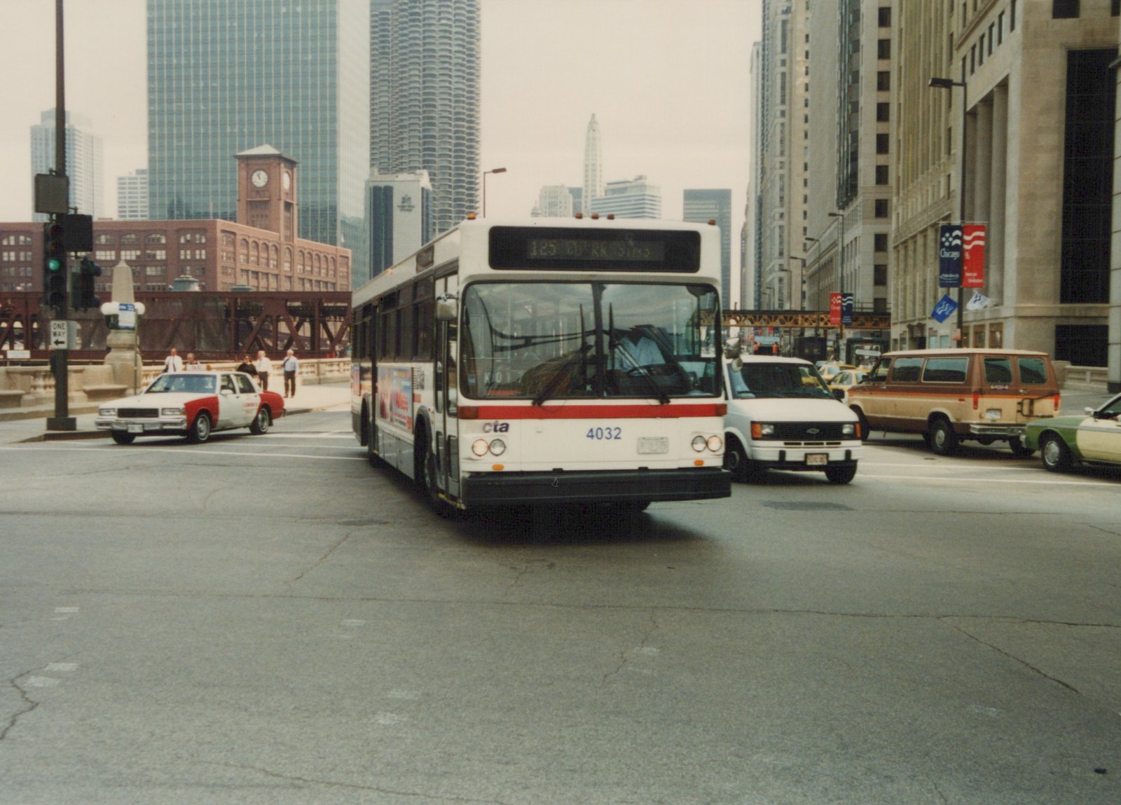 A white and red CTA bus with the number 4032 is stopped at a city intersection with tall buildings and other vehicles in the background.