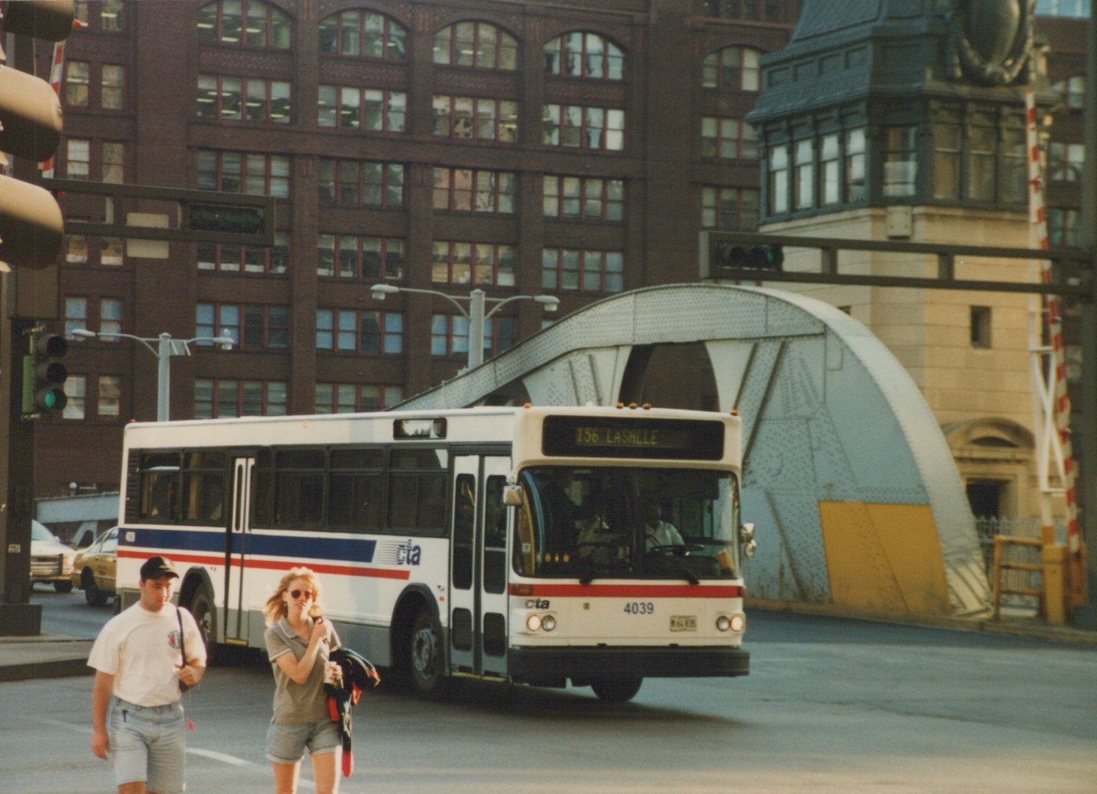 A white and blue Chicago Transit Authority bus, number 4039, is on a city street with a large bridge and pedestrians nearby.
