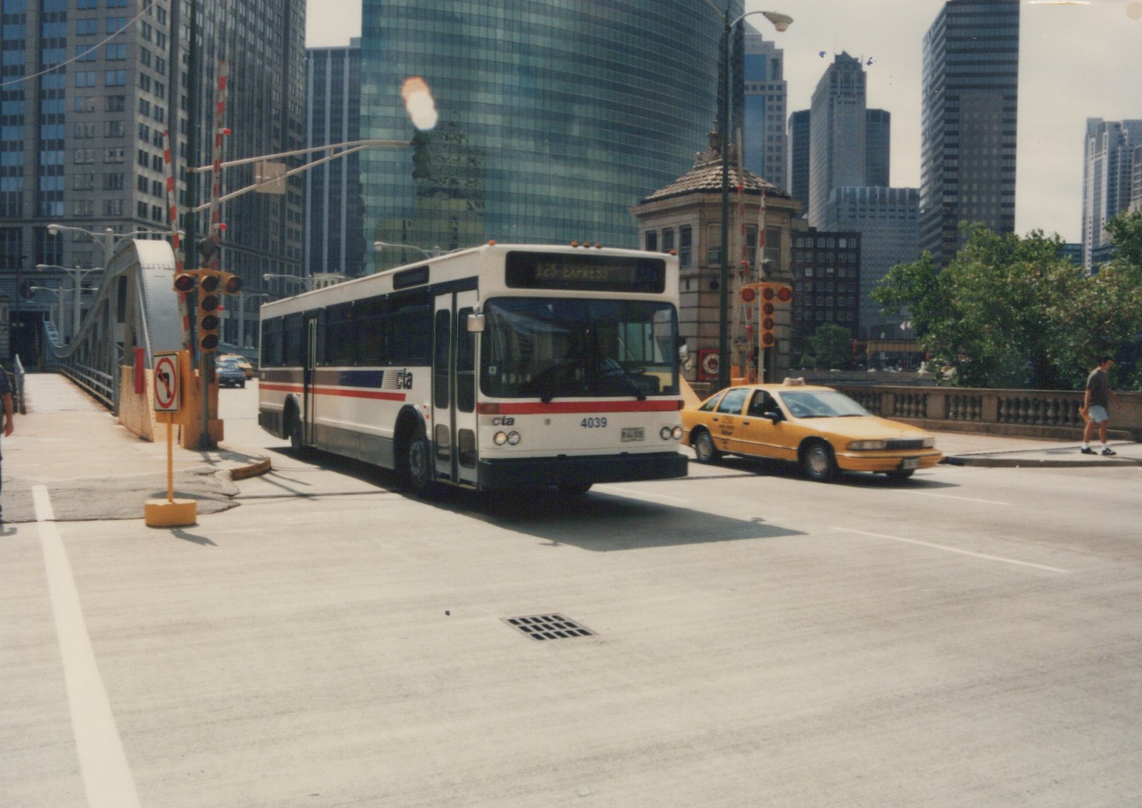 A white and red Chicago Transit Authority motor bus, number 4039, is stopped on a city bridge next to a yellow taxi, with skyscrapers in the background.