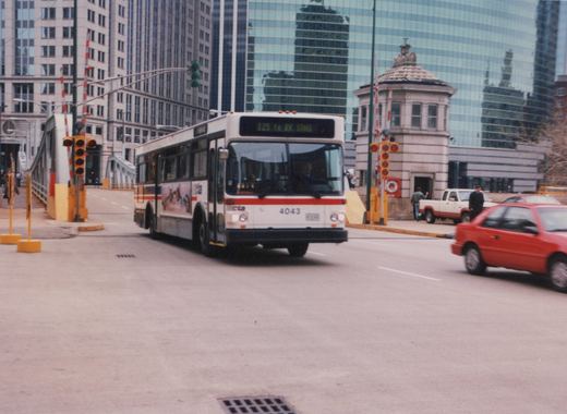 A white and red Chicago Transit Authority bus with the number 4043 on its front, displaying route 125 to R.R. STNS, is driving on a street with a drawbridge and modern buildings in the background.
