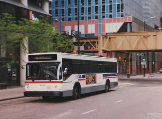 A white CTA bus with the number 4054 is driving on a city street, with a modern building and an elevated structure in the background.