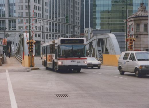 A white and red CTA bus with the number 4063 is driving on a bridge in a city, with tall buildings in the background and other vehicles on the road.
