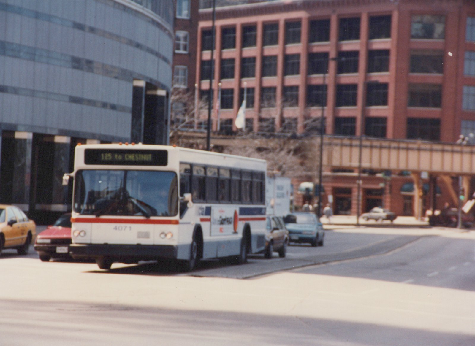 A white and red Chicago Transit Authority bus, number 4071, is stopped at an intersection with several cars and buildings in the background.