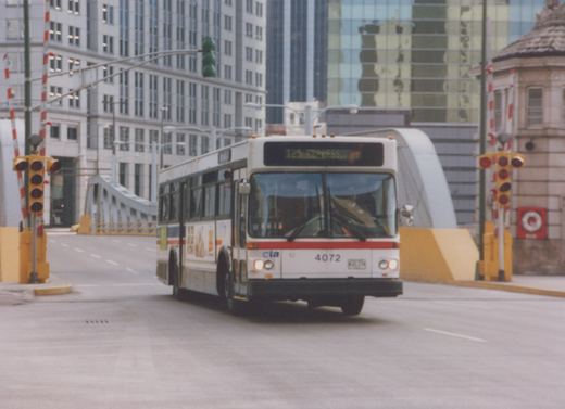 A white and red CTA bus numbered 4072 with a destination sign reading '125 EXPRESS' is driving on a city street near a bridge, with modern buildings in the background.