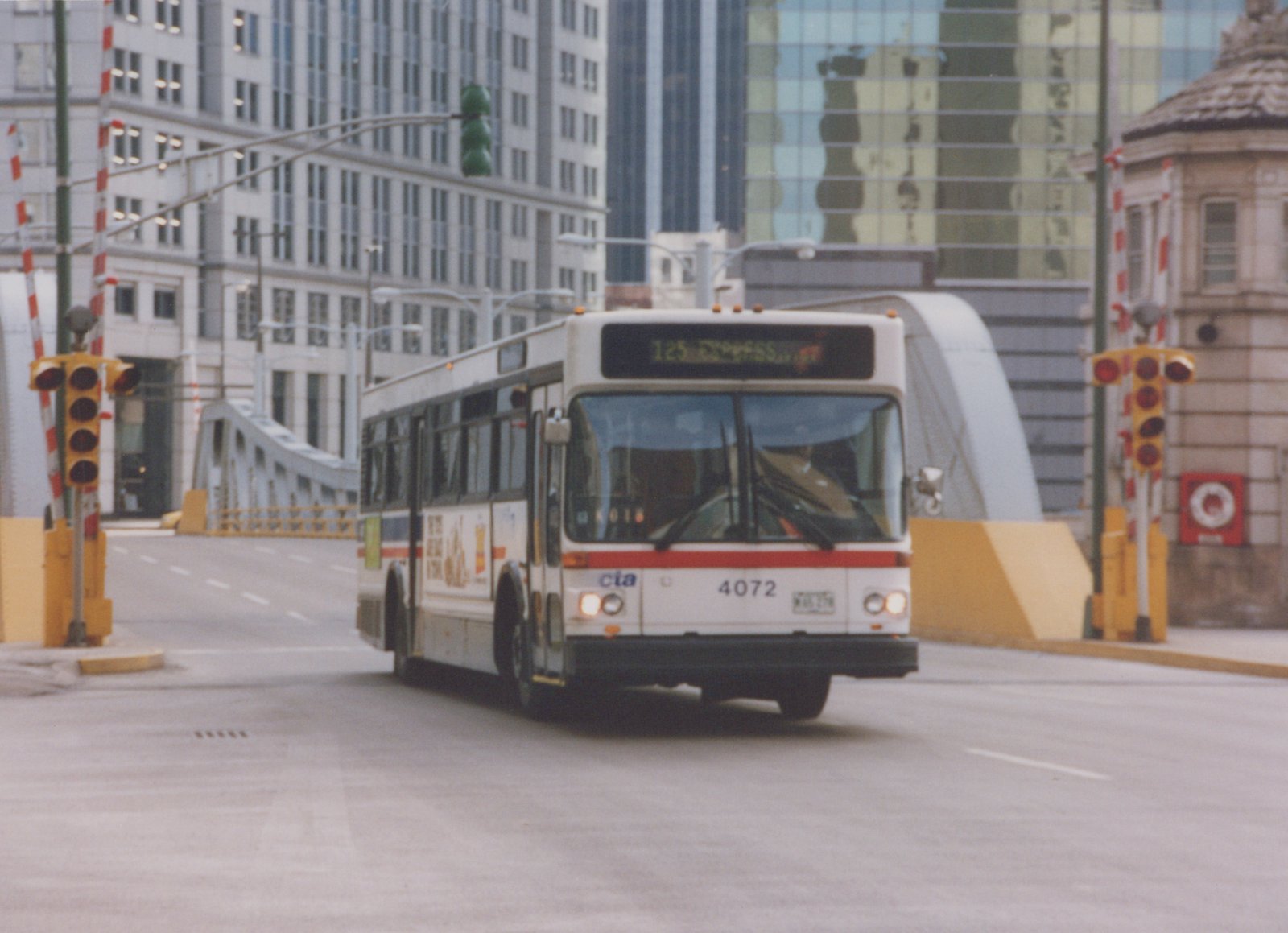 A white and red CTA bus numbered 4072 with a destination sign reading '125 EXPRESS' is driving on a city street near a bridge, with modern buildings in the background.