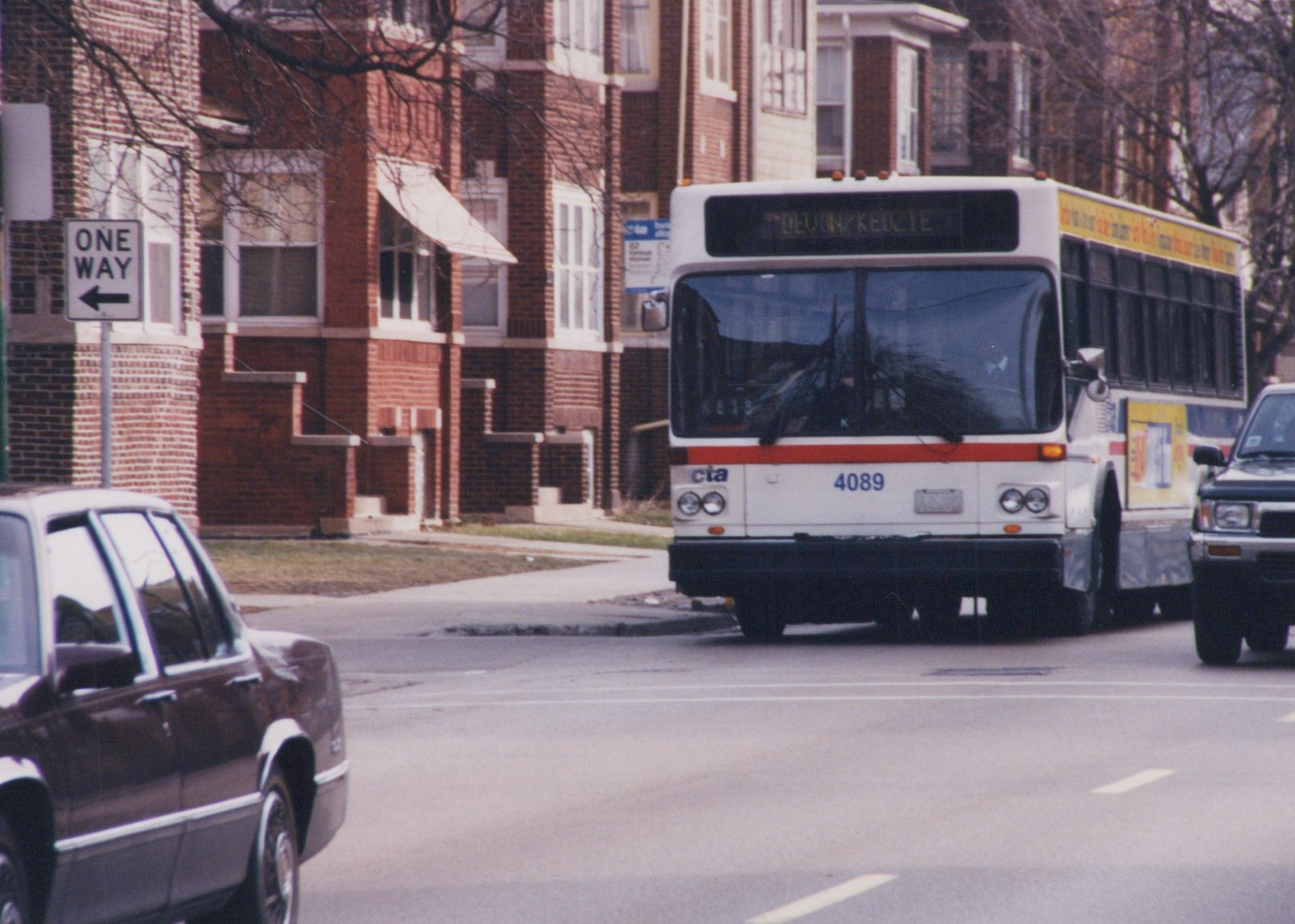 Front view of a white CTA bus with a red stripe, number 4089, on a city street in winter, with a 'ONE WAY' sign and brick buildings in the background.