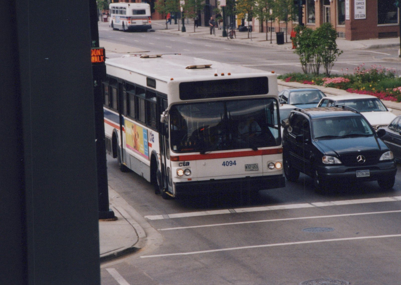 A white, red, and blue Chicago Transit Authority bus, fleet number 4094, is shown from a three-quarter front view as it turns a corner on a city street, with a black Mercedes SUV and other traffic nearby.