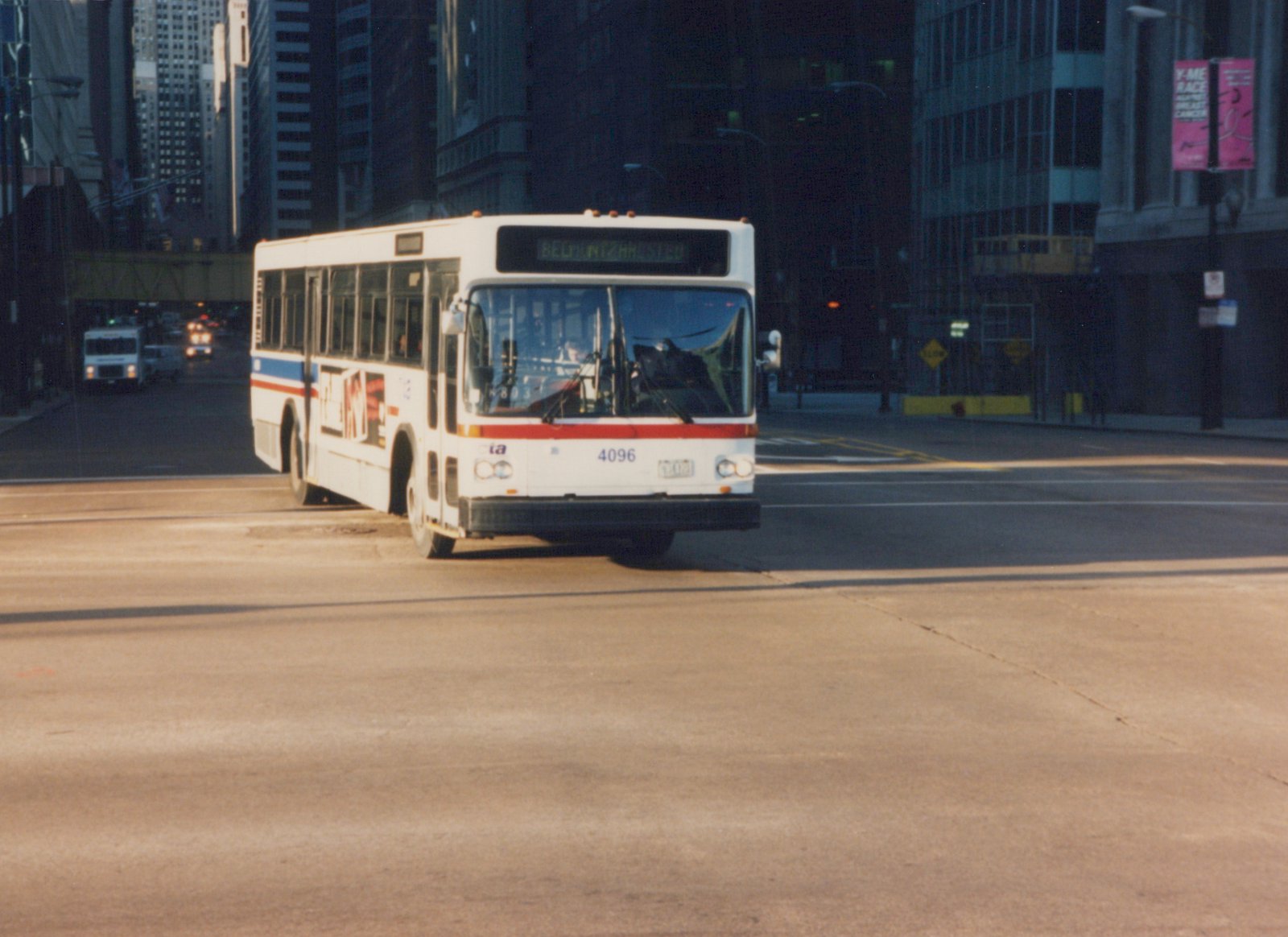 A white, red, and blue Chicago Transit Authority motor bus, number 4096, is driving on a city street with skyscrapers in the background.