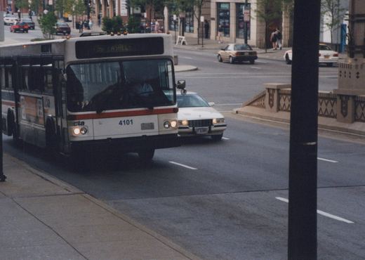 A white and red Chicago Transit Authority bus with the number 4101 on its front is driving on a city street with other cars, surrounded by buildings and pedestrians.