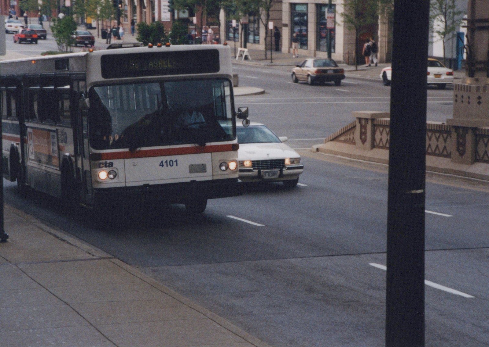A white and red Chicago Transit Authority bus with the number 4101 on its front is driving on a city street with other cars, surrounded by buildings and pedestrians.