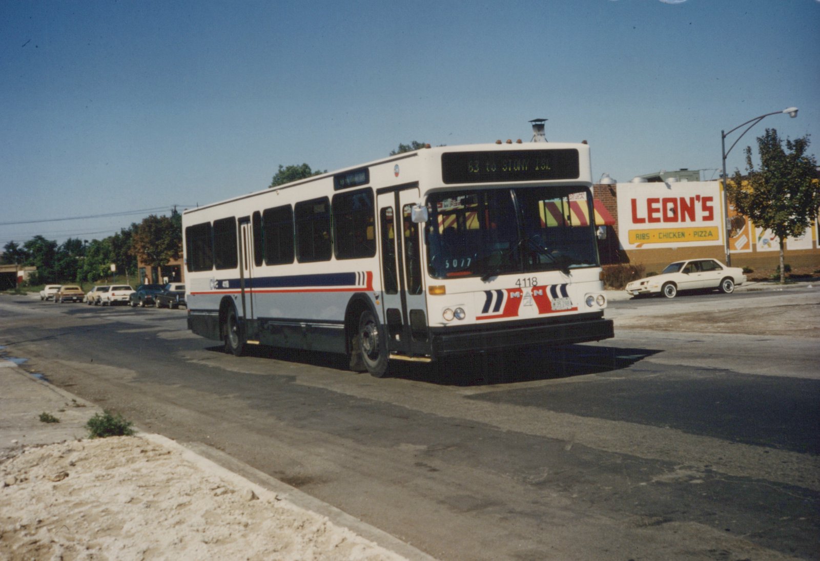 A white Chicago Transit Authority bus with red and blue stripes, numbered 4118, is driving down a street on a clear day with a "Leon's" restaurant sign in the background.