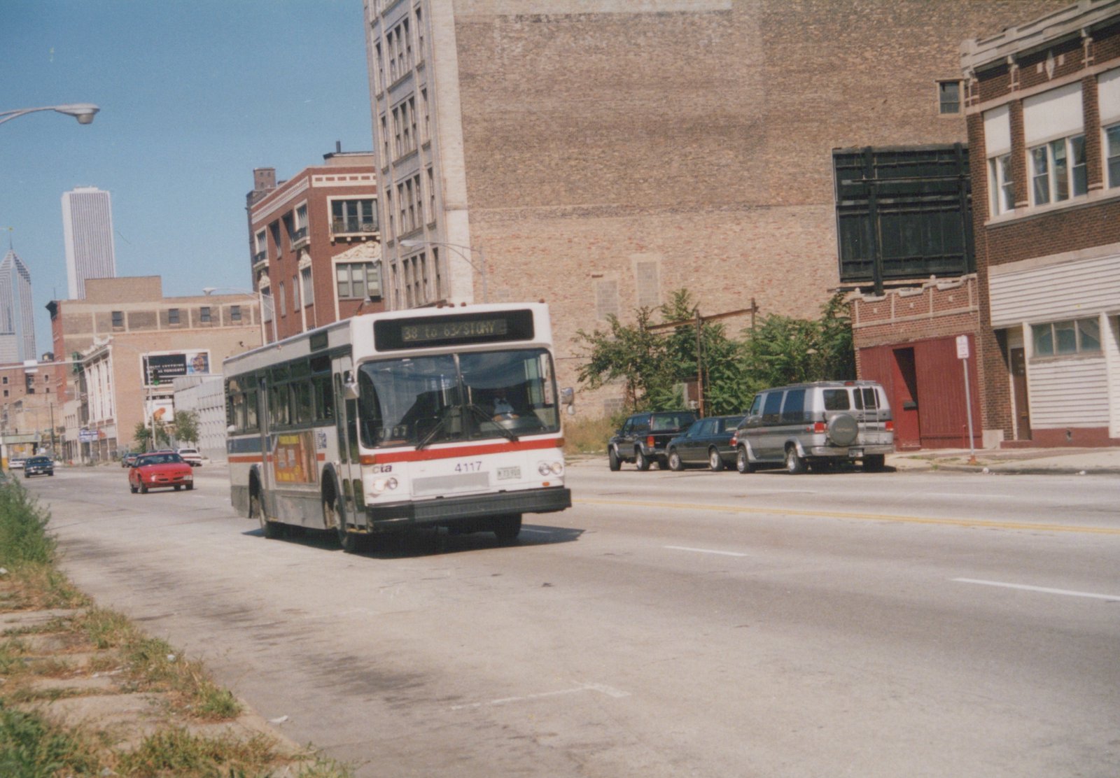 A white, red, and blue Chicago Transit Authority bus is driving down a city street with brick buildings and other cars in the background.