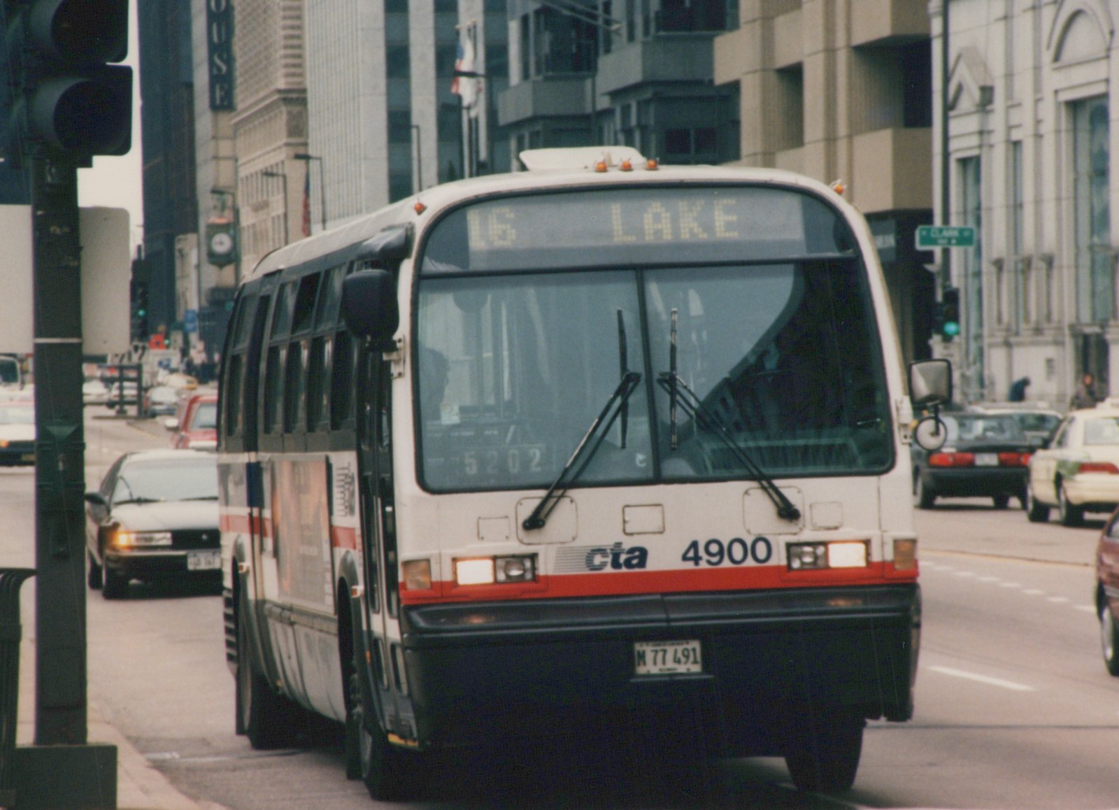 Front-facing view of a white and red CTA bus with number 4900 on a city street, displaying route 16 Lake, with Clark Street sign visible in the background.