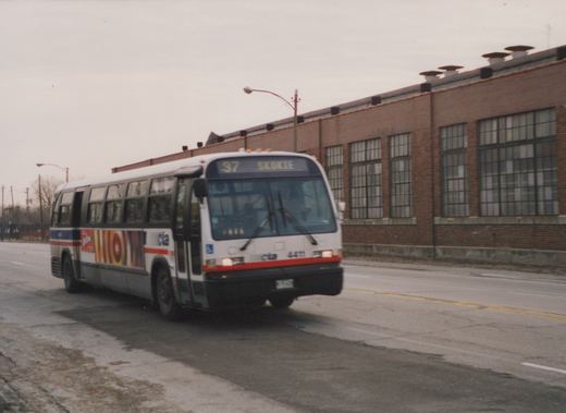 A white Chicago Transit Authority motor bus numbered 4411 is driving down a street in front of a large brick building on an overcast winter day.
