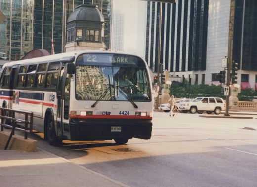 A white Chicago Transit Authority bus with the number 4424 and destination sign reading "22 CLARK" is stopped on a city street with tall buildings in the background.