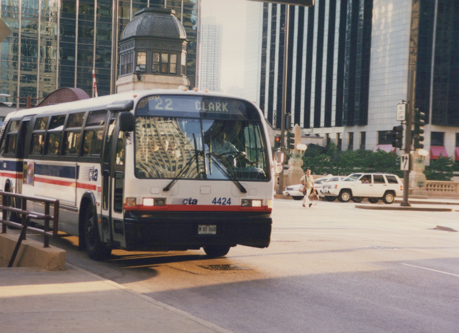A white Chicago Transit Authority bus with the number 4424 and destination sign reading "22 CLARK" is stopped on a city street with tall buildings in the background.