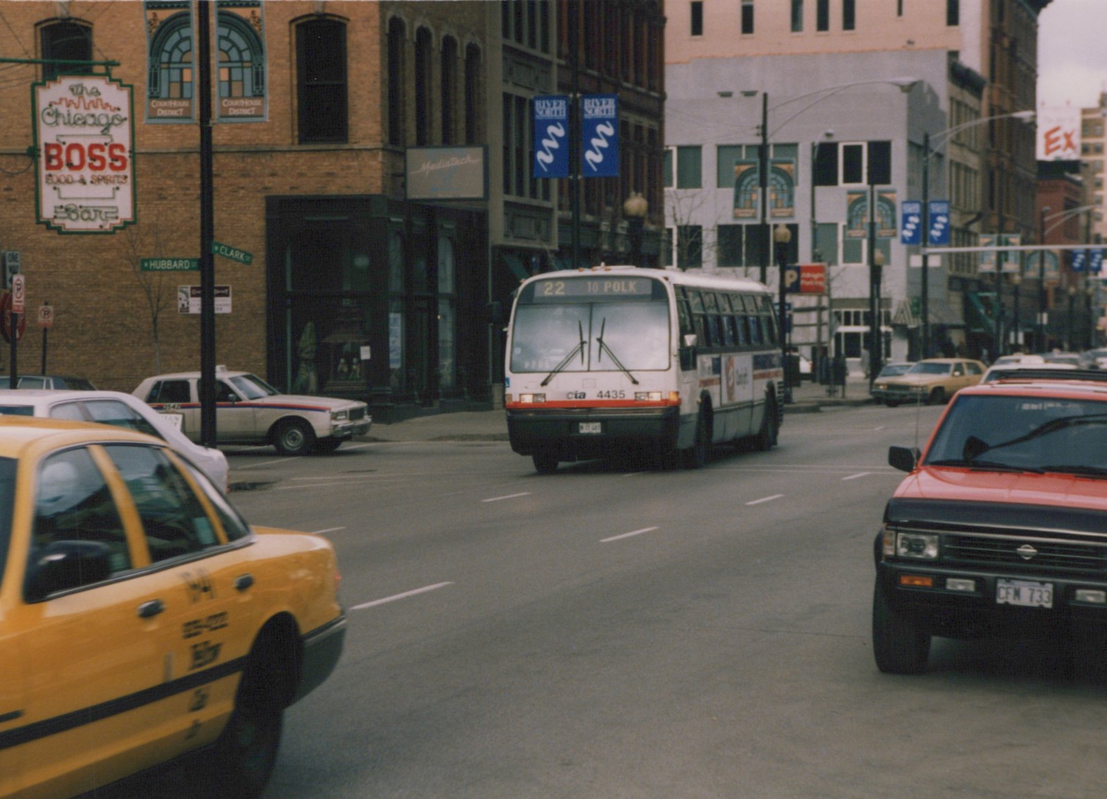 A white and red CTA bus with the number 4435 is driving down a city street, with street signs for Hubbard and Clark streets visible, alongside parked cars and a yellow taxi.