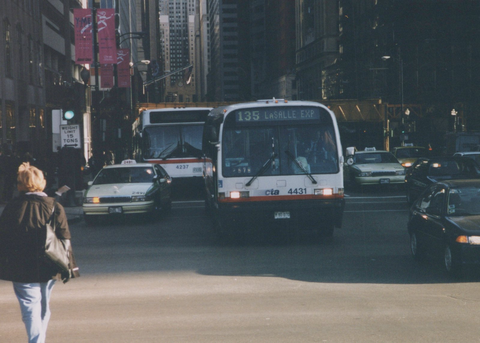 A front view of a white CTA bus numbered 4431 with a '135 LASALLE EXP' destination sign, accompanied by another CTA bus and several taxis on a busy city street.