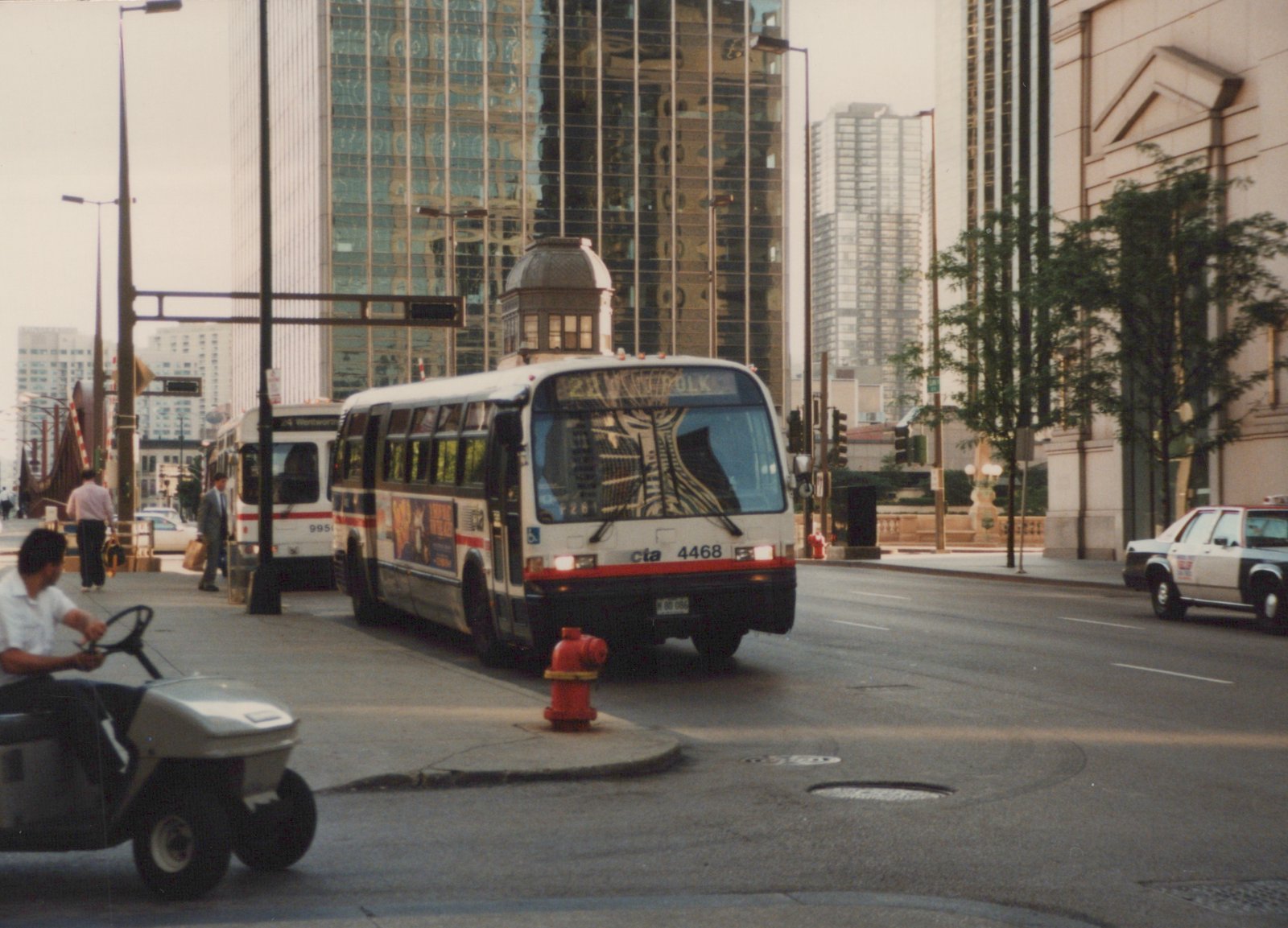 A white and red Chicago Transit Authority bus, number 4468, is driving on a city street with tall buildings in the background. Another CTA bus and a police car are visible behind it.