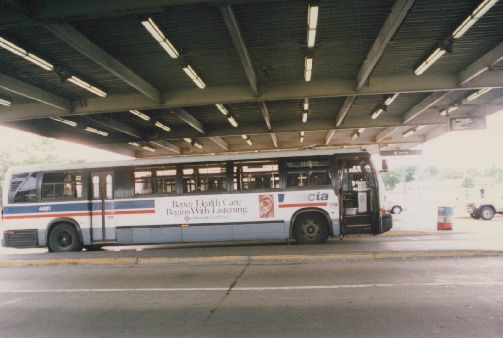 A side view of a white CTA bus with blue and red stripes, number 4481, parked under a covered station with its doors open, showing a route sign for 90 Harlem.