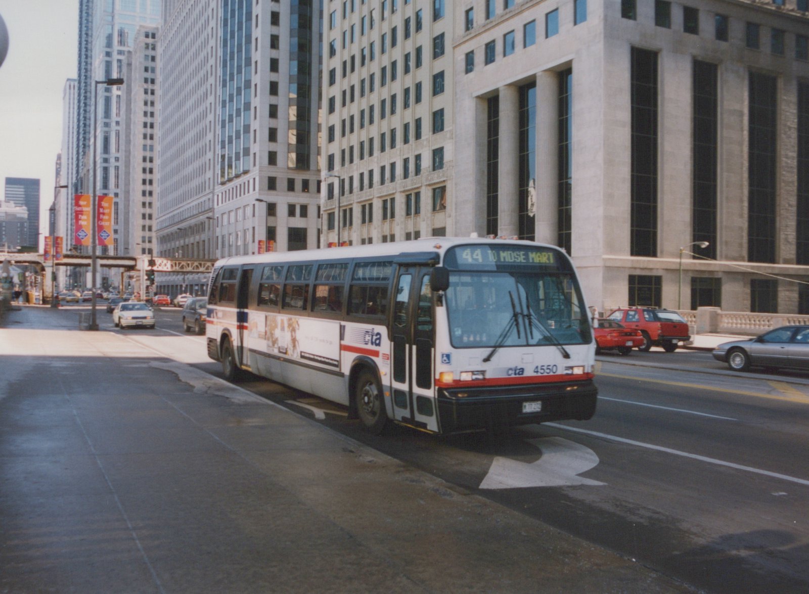 A white, red, and blue Chicago Transit Authority bus numbered 4550 is turning on a city street with tall buildings in the background.