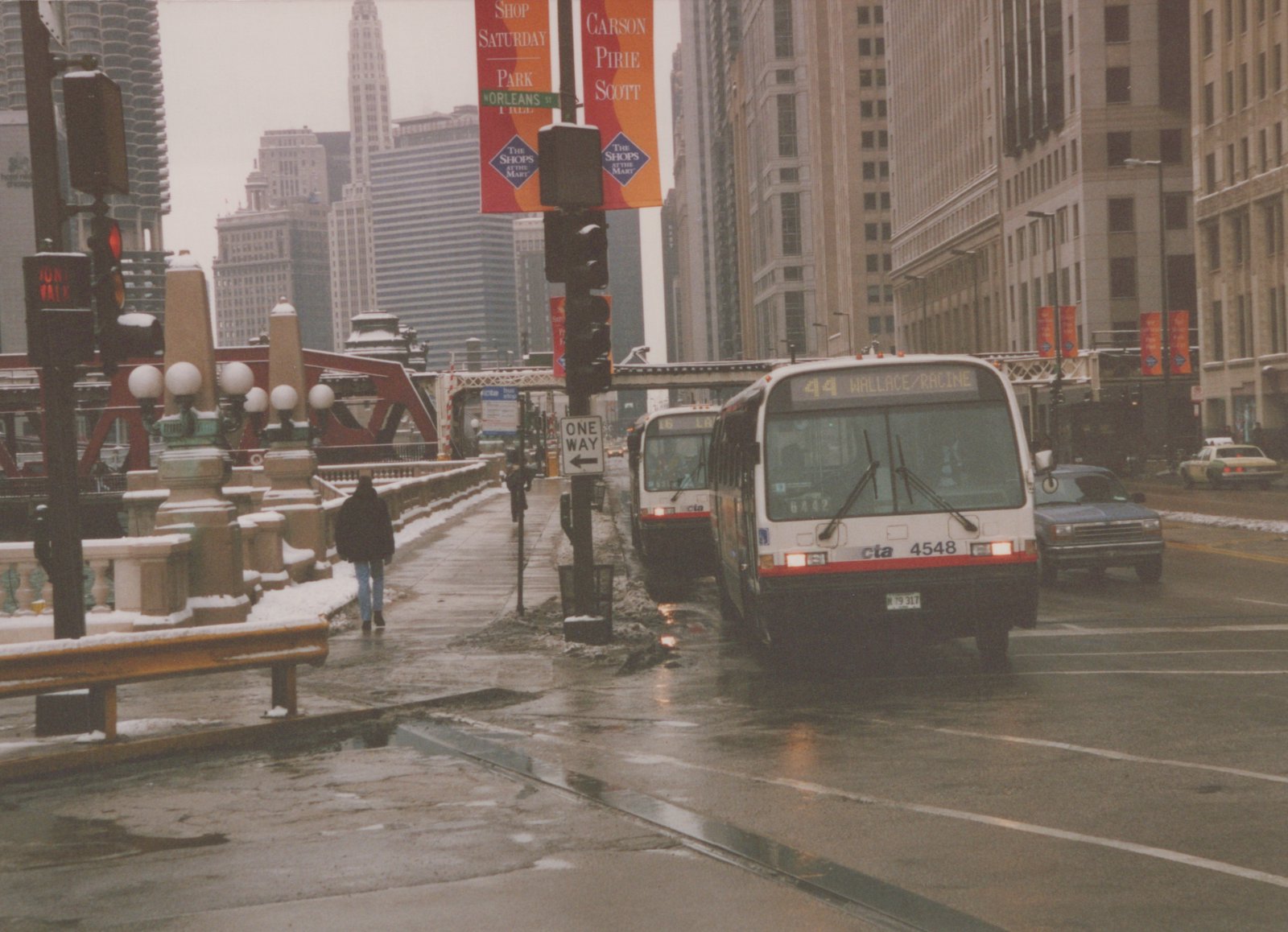 Two white and red Chicago Transit Authority buses on a wet, snowy city street with tall buildings and pedestrians, one bus showing route 44 and number 4548.