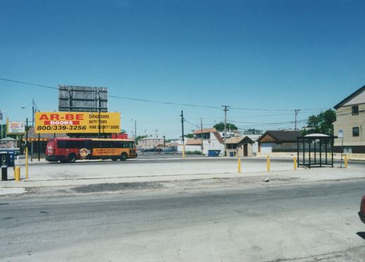 A red and orange Chicago Transit Authority bus, number 5567, with Hard Rock Cafe advertising, is parked on a street under a clear blue sky next to a large yellow billboard.