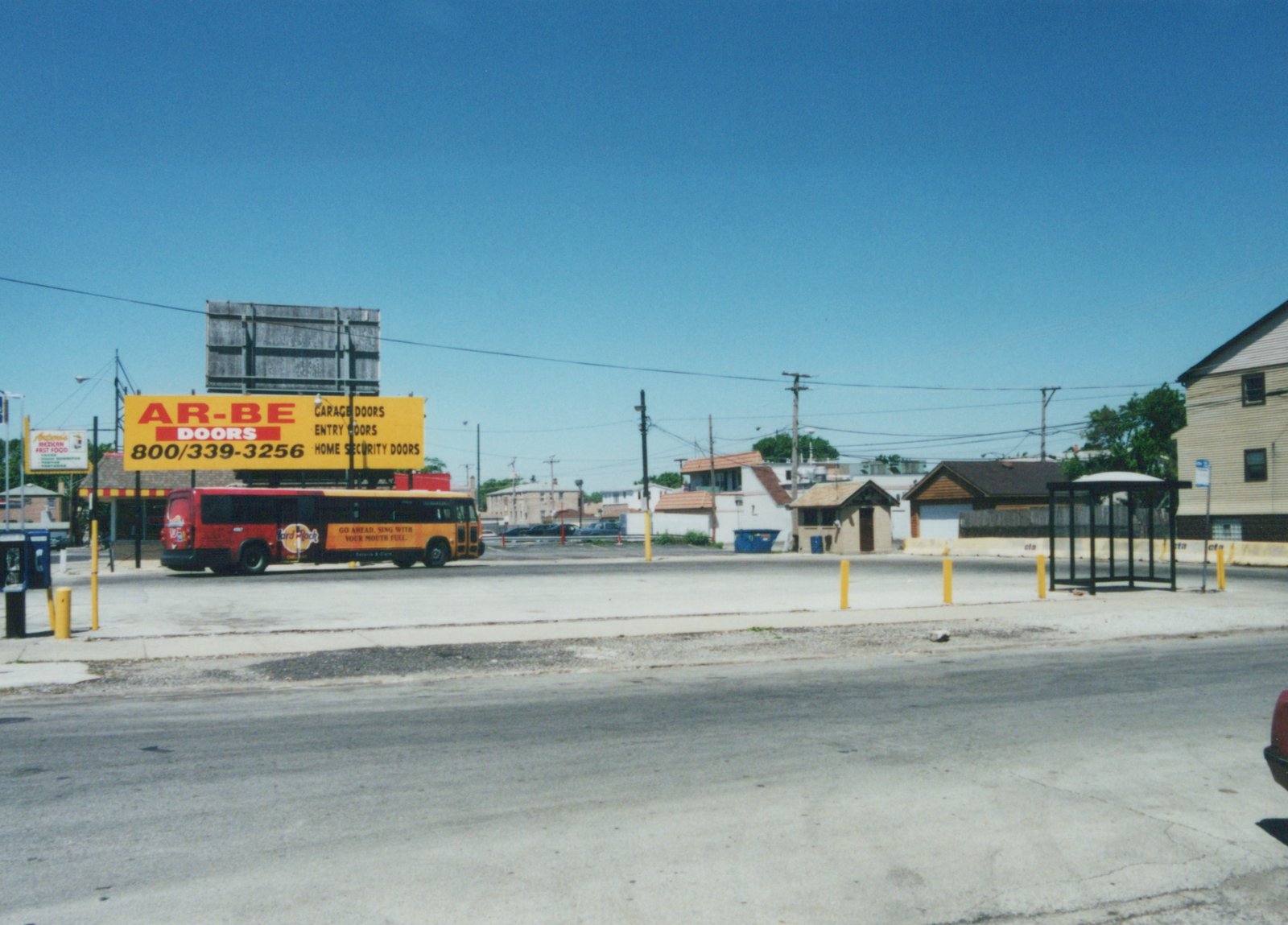 A red and orange Chicago Transit Authority bus, number 5567, with Hard Rock Cafe advertising, is parked on a street under a clear blue sky next to a large yellow billboard.