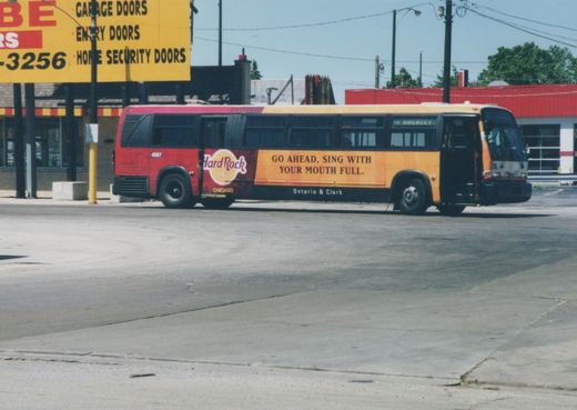 A red and yellow Chicago Transit Authority bus with a Hard Rock Cafe ad is parked on a street on a sunny day.
