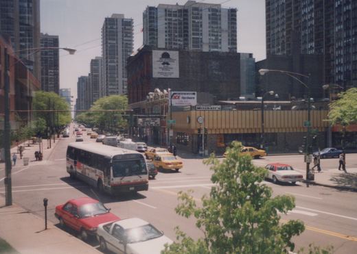 A white and red CTA bus numbered 4571, displaying route 22 Clark, drives down a city street lined with tall buildings and other vehicles, including yellow taxis and sedans, under a clear sky.