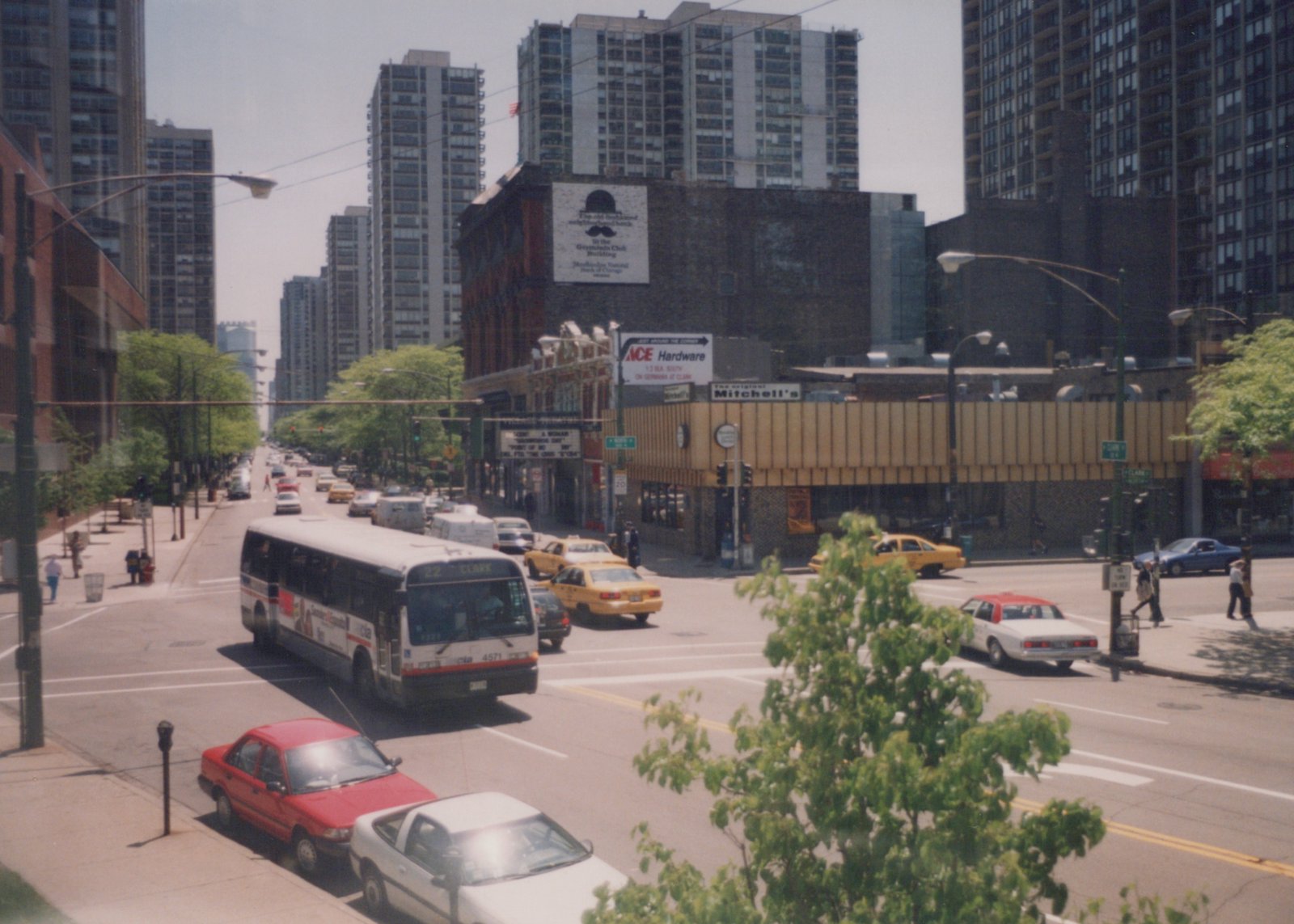 A white and red CTA bus numbered 4571, displaying route 22 Clark, drives down a city street lined with tall buildings and other vehicles, including yellow taxis and sedans, under a clear sky.