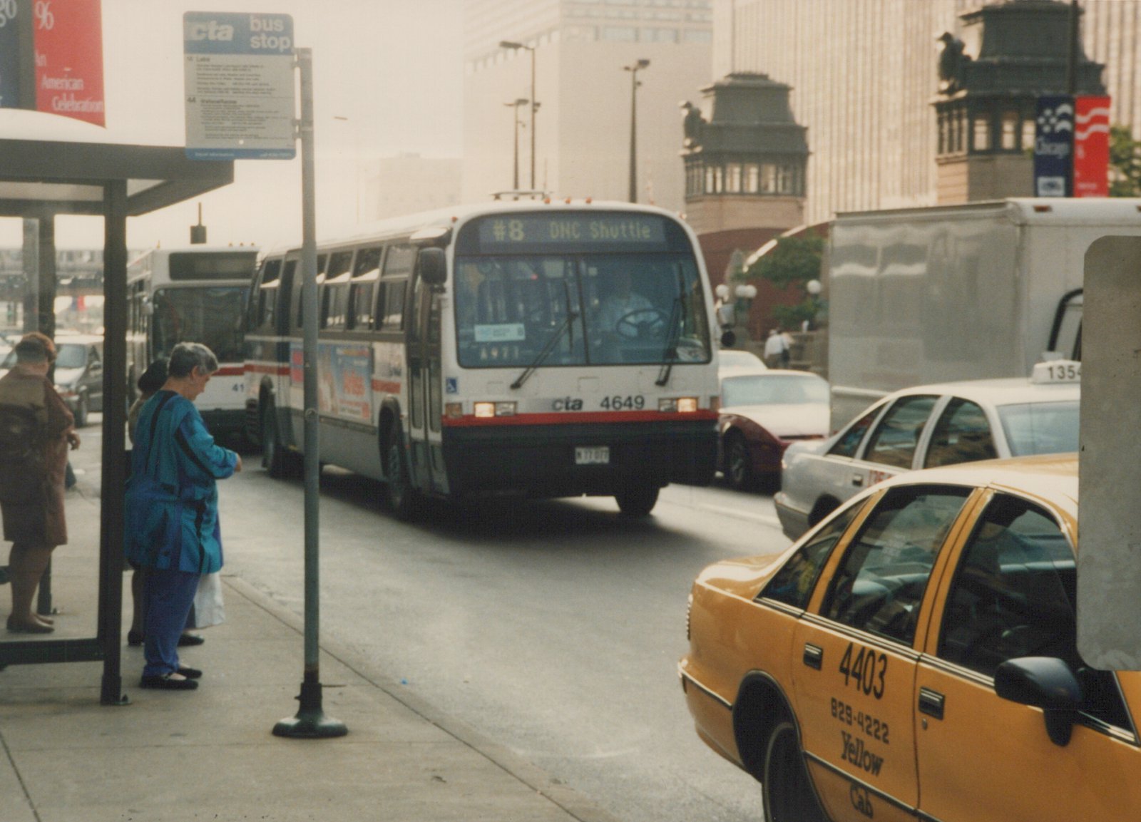 A white and red Chicago Transit Authority bus with the number 4649 is stopped on a city street next to a bus stop where people are waiting; yellow and white taxis are visible in the foreground and background.