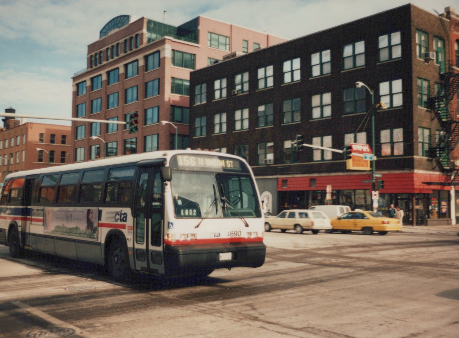 A white, red, and blue CTA bus, number 4690, is turning on a city street with tall buildings in the background.