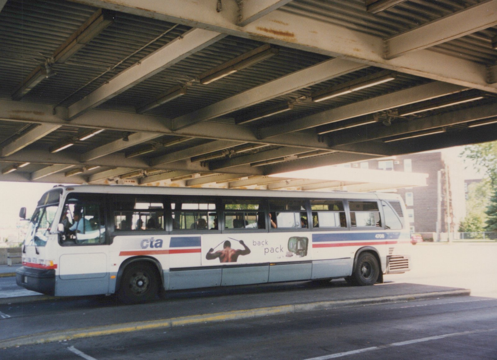 A white and blue Chicago Transit Authority bus, number 4708, is parked on a street under a steel bridge, with passengers visible inside.